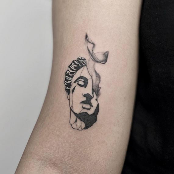 greek broken face sculpture tattoo female lower bicep