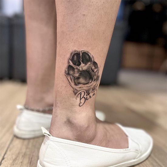 small dog paw with name bira tattoo woman leg ankle