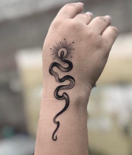 minimalist snake with sun tattoo design woman wrist